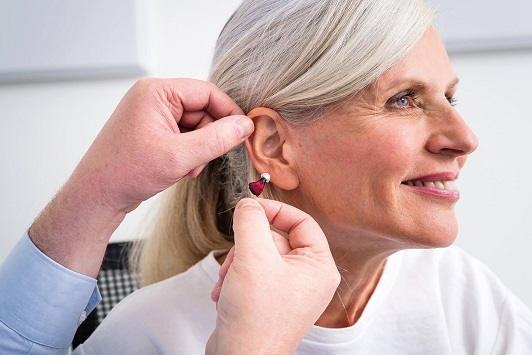 Ältere Frau bekommt ein modernes Hörgerät angepasst, Hörakustiker unterstützt Beratung.